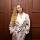 Vrouw met lang blond haar, staand in satijnen badjas met witte fleece kraag.