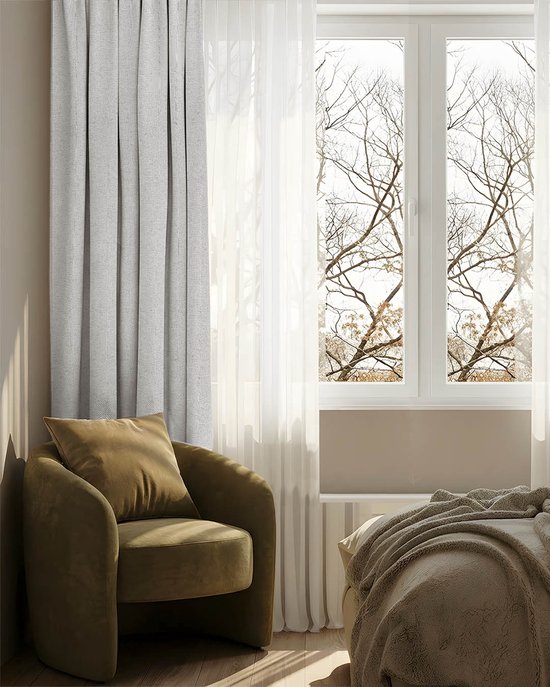 Een stijlvolle woonkamer met een lichtgrijs gordijn dat voor een raam hangt, met een fauteuil en een bed.