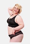 Model met blonde krullen draagt een zwarte kanten bralette en slip.