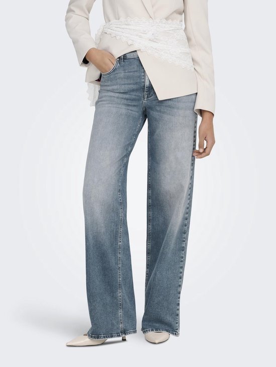 Model in een blauwe spijkerbroek met wijde pijpen en een beige blazer, met kanten detail.