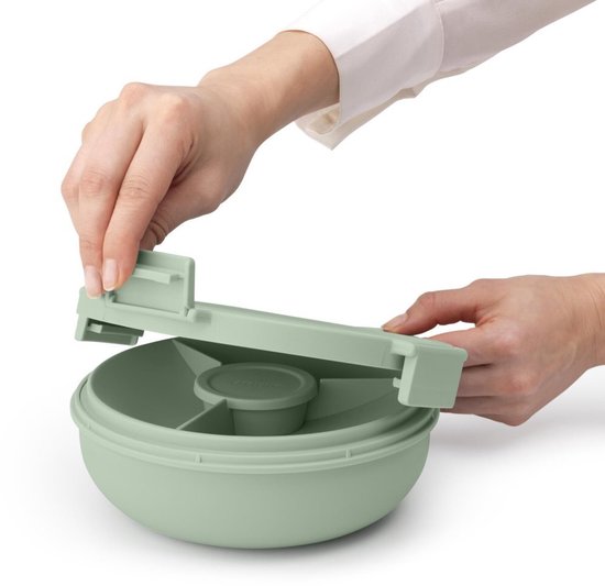 Mains plaçant le couvercle sur une boîte à salade vert pâle avec diviseur et pot à vinaigrette.