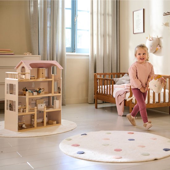 Klein meisje met roze kleding dat een poppenhuis van hout met roze dak bekijkt in een kinderkamer.