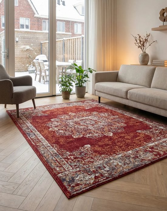 Rood vloerkleed met vintage patroon op een houten vloer, met bank en stoel.
