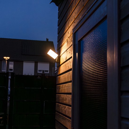 Zwarte wandlamp met sensor, verlicht de houten schutting en een raam.