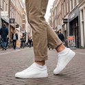 Man met een beige broek en witte sneakers, witte lage sokken, op een kasseienstraat.
