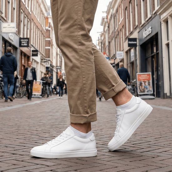 Man met een beige broek en witte sneakers, witte lage sokken, op een kasseienstraat.