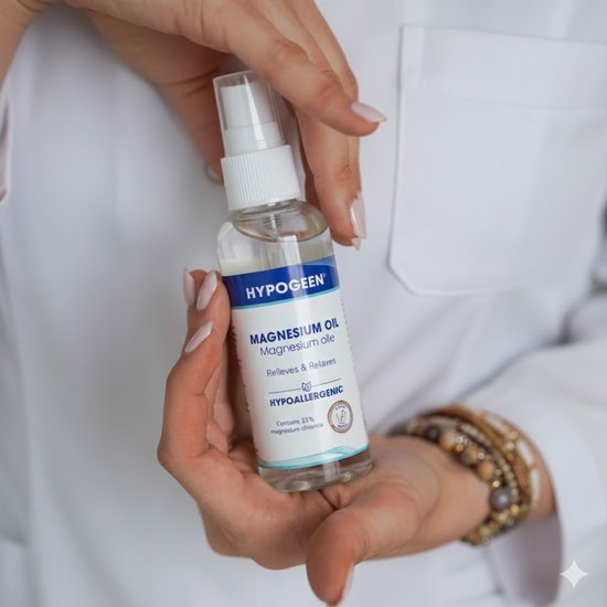 Gedetailleerde foto van een flesje Hypogeen magnesiumolie spray in een hand. Etiket toont 'Magnesium olie', 'Relieves & Relaxes', 'Hypoallergeen' en 'Contains 33% magnesium chloride'.