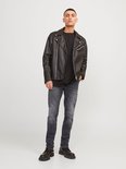 Man met zwart T-shirt, zwarte leren bikerjack en grijze jeans.