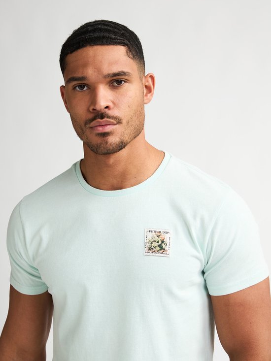 Close-up van een lichtgroen T-shirt met een opgedrukte postzegel met bloemen.