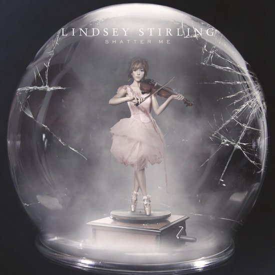 Lindsey Stirling in een roze jurk met ballerina schoenen staat op een draaiplateau in een gebroken glazen bol.