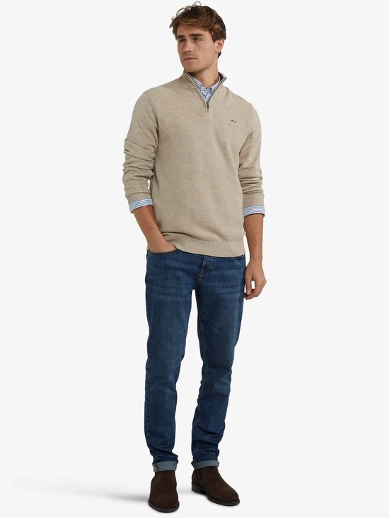 Man draagt beige trui met ritssluiting en spijkerbroek.