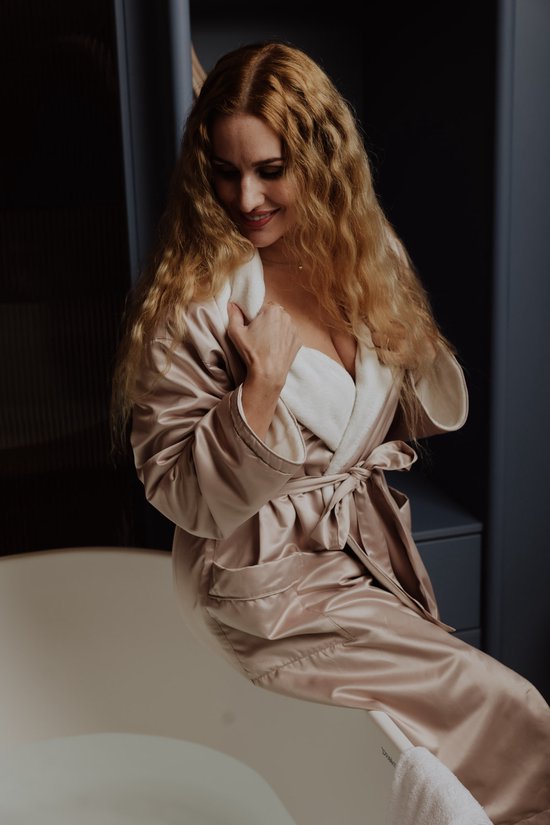 Vrouw in satijnen badjas met witte fleece voering bij een badkuip.