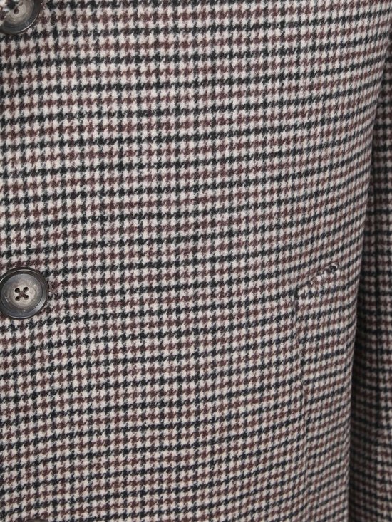 Detail van een bruin-grijze jas met pied-de-poule patroon en knoop.