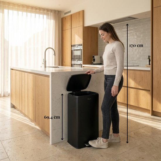 Vrouw staat naast een zwarte Bayt prullenbak van 69.4 cm hoog in een keuken, met afmetingen aangegeven.