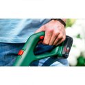 Man houdt de groene handgreep van de Bosch grastrimmer vast, met rode knoppen en accu.