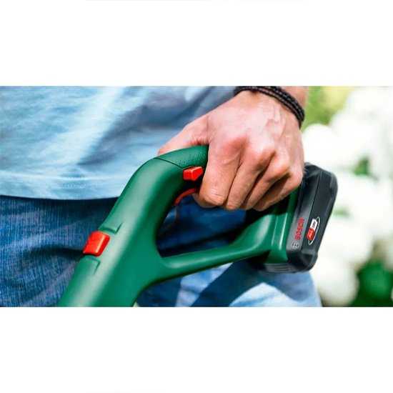Man houdt de groene handgreep van de Bosch grastrimmer vast, met rode knoppen en accu.
