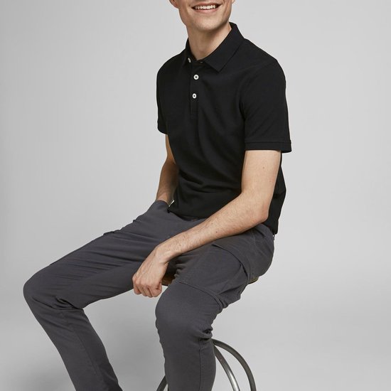 Zwarte polo met korte mouwen, gedragen door een man zittend op een kruk.