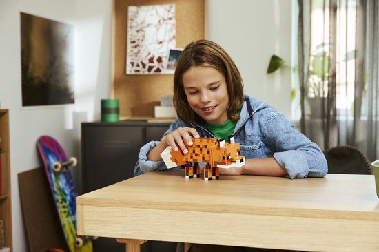 Un garçon à une table en bois joue avec un renard LEGO Minecraft constructible.