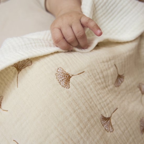 Witte hydrofiele deken met bruine ginkgo bladeren print, babyhandje op de deken.