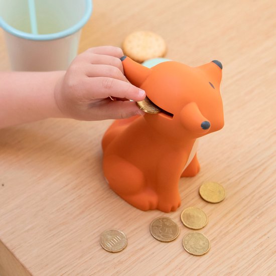 Kind steekt muntje in oranje vossen spaarpot. Munten op houten ondergrond.