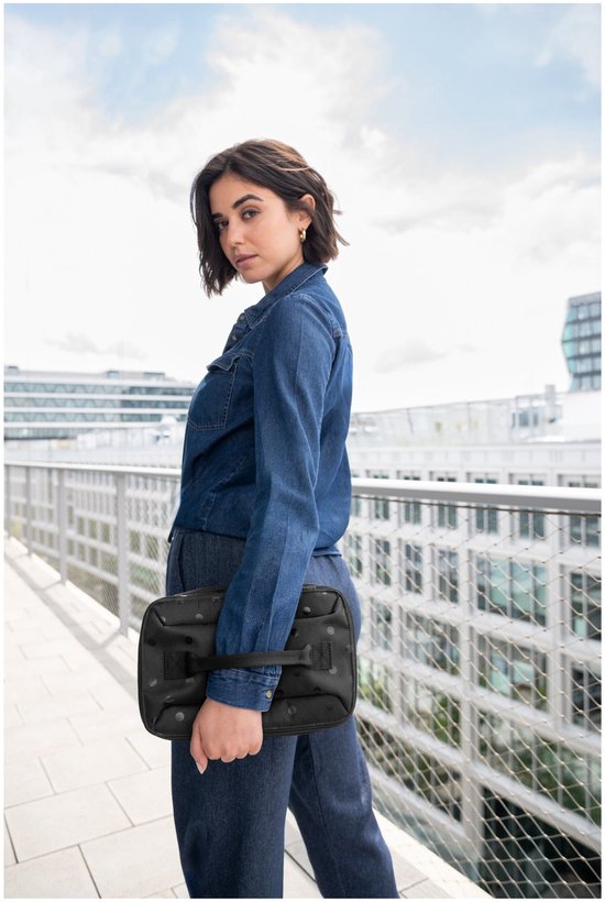 Vrouw met sproeten, gekleed in een spijkerblouse, draagt een zwarte toilettas met stippen.