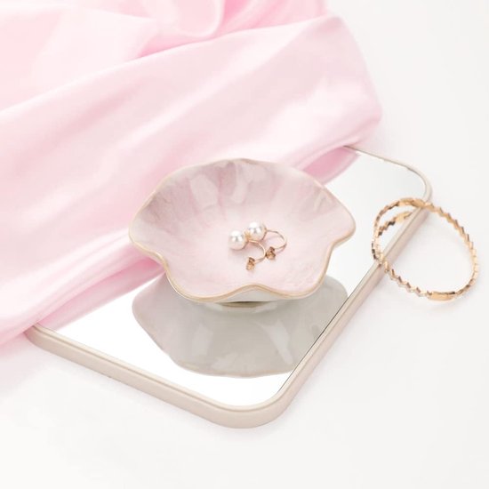 Roze keramische schaal met marmerpatroon en parelmoer oorbellen, naast een spiegel en gouden armband.