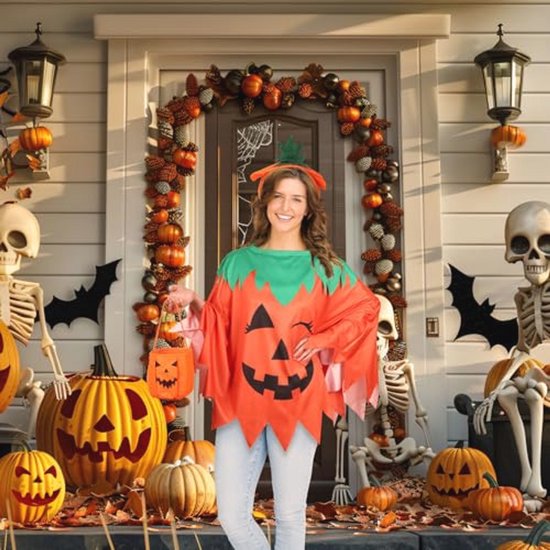 Vrouw in oranje pompoencape voor een deur versierd met herfstbladeren, schedels en pompoenen.