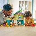 Un père et un enfant jouent avec une maison de jeu LEGO Duplo, aux murs verts, violets et vert clair.