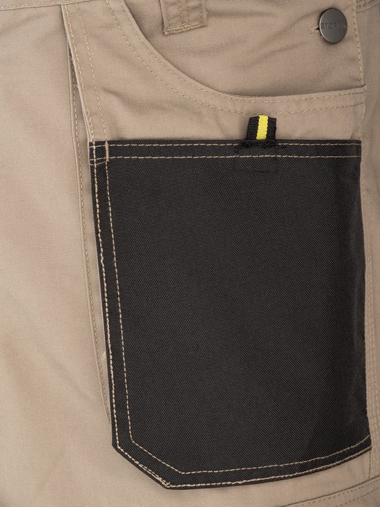 Salopette beige avec une poche noire et une boucle jaune et noire, avec un bouton STØRVIK.