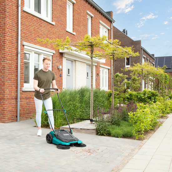Man met groen T-shirt veegt met turquoise veegmachine over betegeld pad.