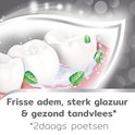 Witte tanden met roze tandvlees, omringd door water en muntblaadjes.