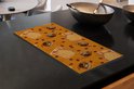Oranje kookplaatbeschermer met illustraties van koffiekopjes en -bonen op een aanrecht.