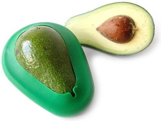 Een halve avocado met pit naast een groene bewaardoos waarin een hele avocado past.