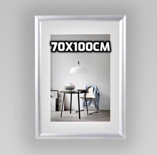 Cadre argenté 70x100cm avec une photo d'intérieur d'une table, d'une chaise et d'une lampe.