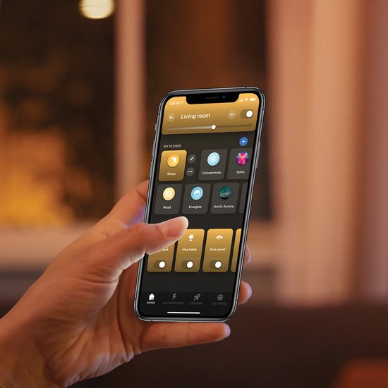 Hand met smartphone met Philips Hue app, toont scènes zoals Relax, Concentrate en Soho.