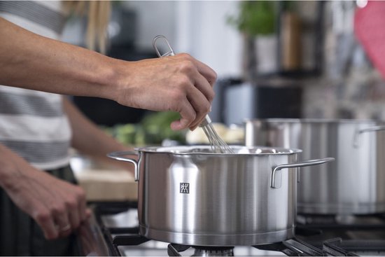 Persoon in de keuken die in een roestvrijstalen kookpot roert met een garde.
