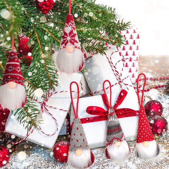 Nains de Noël avec des bonnets tricotés à motifs en rouge, gris et blanc, suspendus à côté de cadeaux sous un sapin de Noël.
