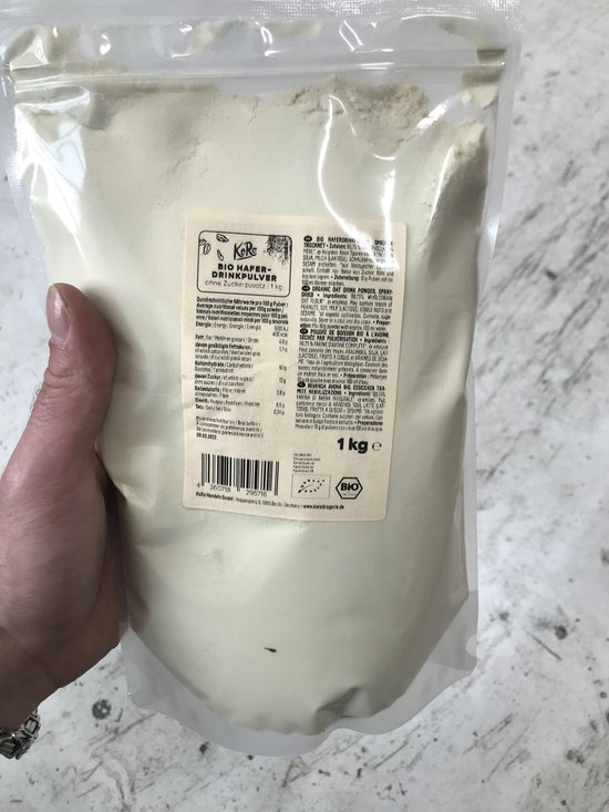 Een hand houdt een zak met 1 kg bio haverdrankpoeder van KoRo vast.