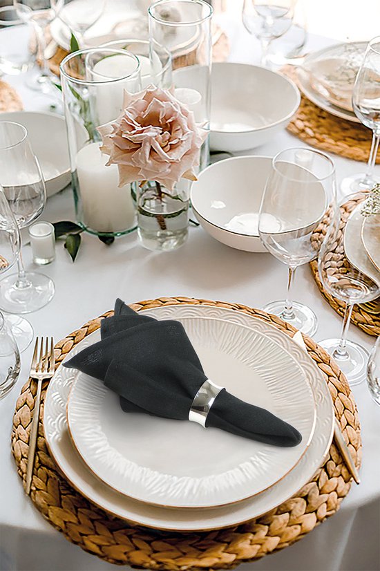 Zwart gevouwen servet met zilverkleurige ring op een gedekte tafel.