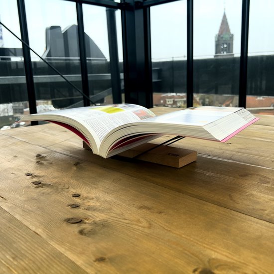 Open boek met roze en rode kaft op houten boekenstandaard, op een tafel.