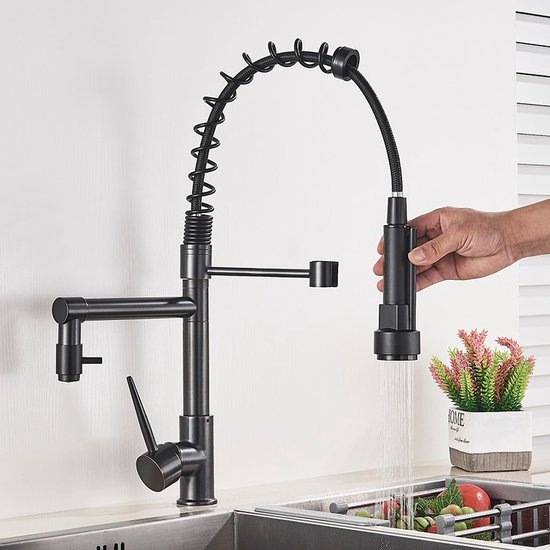 Zwarte keukenkraan met spiraalslang, bediend door een hand die de sproeikop vasthoudt. Water stroomt.