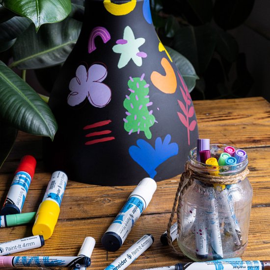 Zwarte lampenkap met kleurrijke, abstracte vormen. Meerdere stiften liggen verspreid.