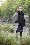 Model draagt een lichtgrijs gebreid vest met twee steekzakken en een zwarte sjaal.