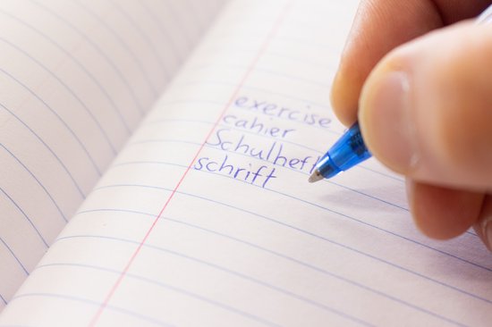 Hand schrijft 'Schulheft' met een blauwe pen in een schrift met lijntjes.