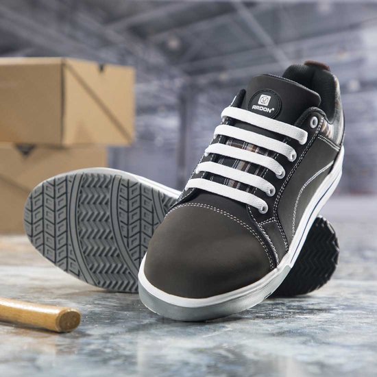 Zwarte Ardon werkschoenen met witte veters en grijs met bruin geruit detail. Staan op een werkplaatsvloer.