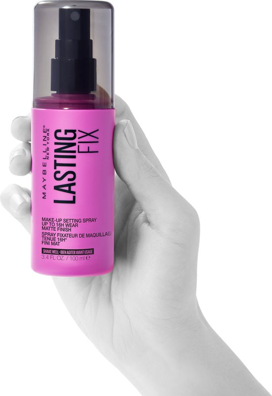 Hand die een Maybelline New York Lasting Fix make-up setting spray vasthoudt, fuchsia fles met transparante dop. Text: "LASTING FIX", "MAKE-UP SETTING SPRAY UP TO 16H WEAR", "MATTE FINISH".
