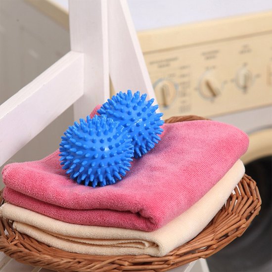 Deux boules de sèche-linge bleues avec des picots sur une pile de serviettes roses et beiges dans un panier.