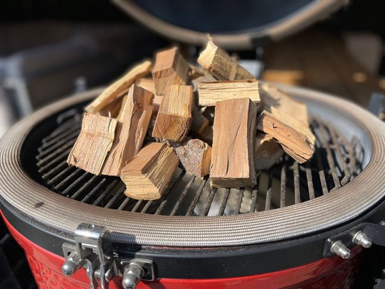 Kersenhouten rookblokken voor de BBQ op een zwart grillrooster in een rode kamado.