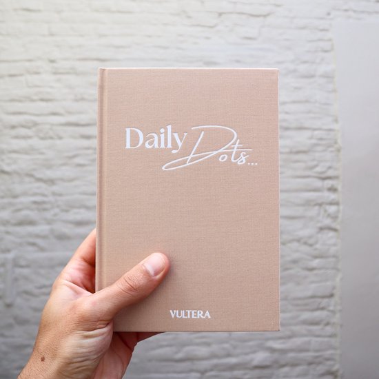 Hand houdt beige notitieboek met "Daily Dots..." en "VULTERA" op de omslag.