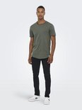 Man met tatoeage op arm, gekleed in groen T-shirt en zwarte slim-fit broek.